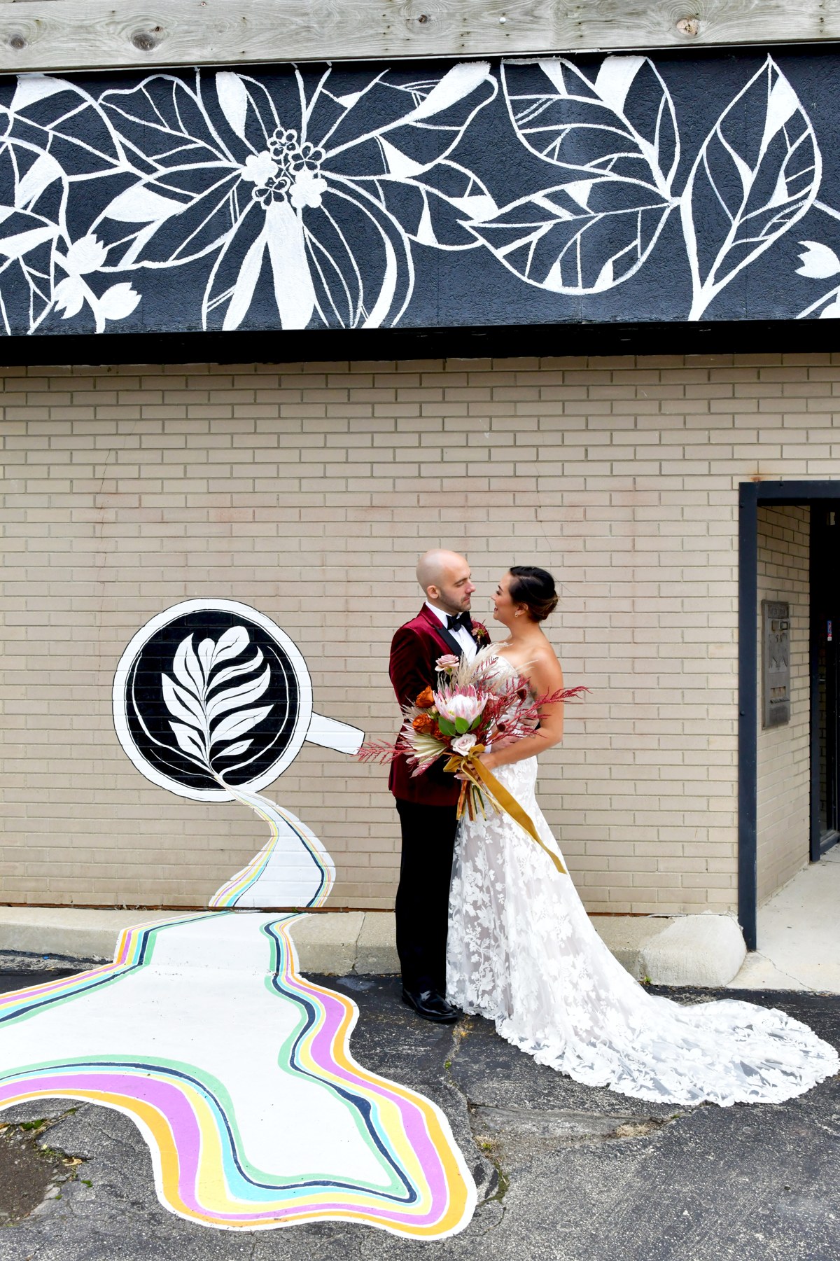 A wedding couple beside the colorful floral mural