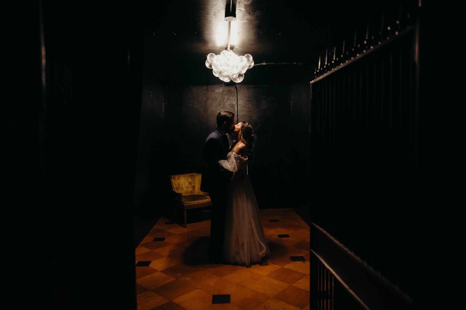 A couple inside the historic dark bank vault beneath a chandelier
